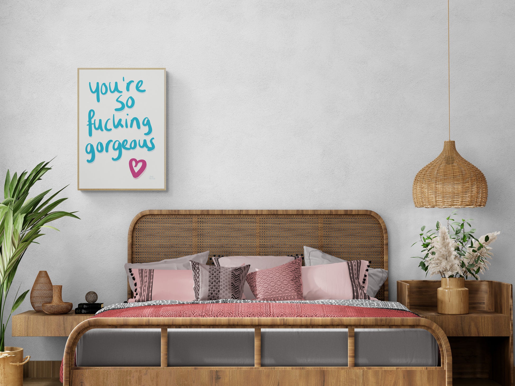 Poster with ‘You’re so fucking gorgeous’ in blue handwriting with a pink heart on a white background. Hanging in a boho style bedroom in an oak frame.