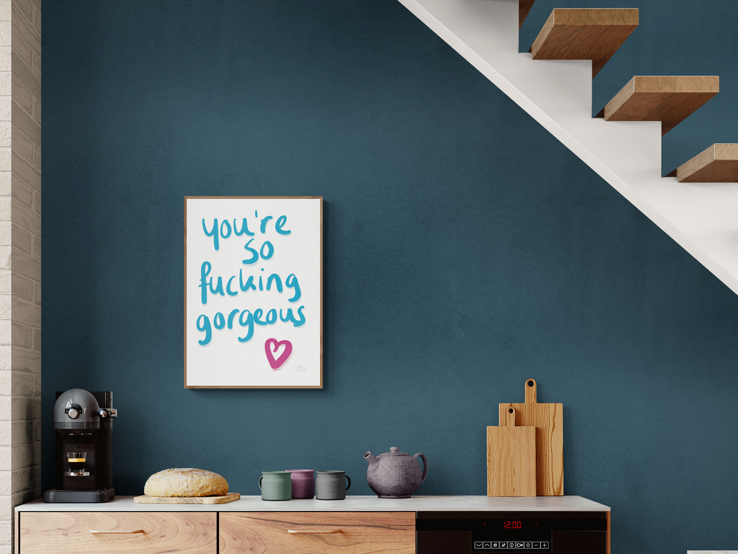 Poster with ‘You’re so fucking gorgeous’ in blue handwriting with a pink heart on a white background. Hanging on a teal wall in a scandinavian style kitchen