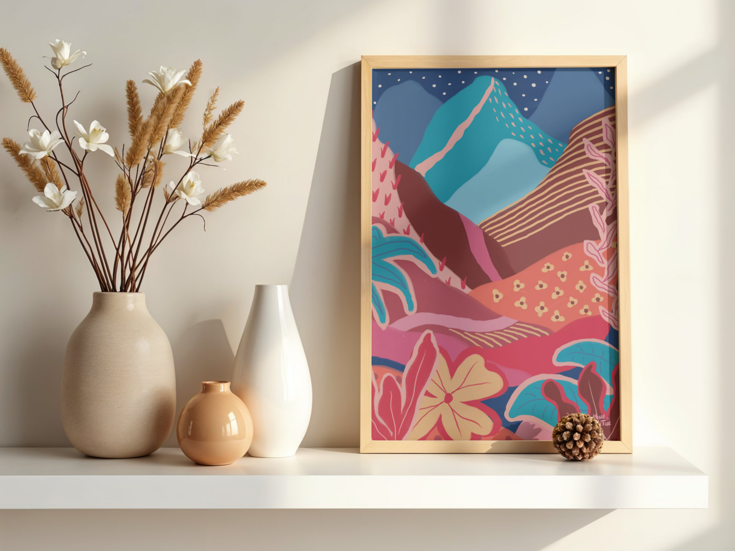 Colourful landscape poster with mountains, sun and tropical plants. Warm, layered wall art in oak frame standing on a white shelf.
