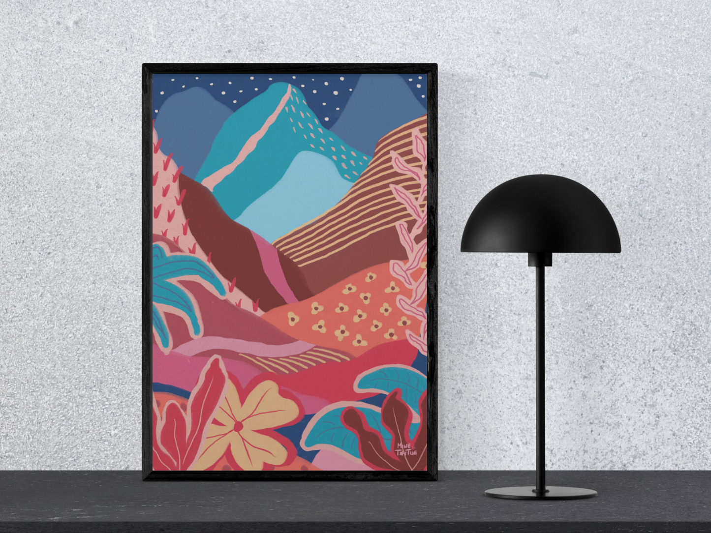Colourful landscape poster with mountains, sun and tropical plants. Warm, layered wall art in black frame standing on desk