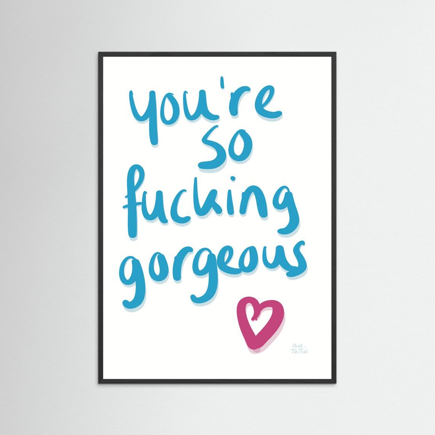 Poster with ‘You’re so fucking gorgeous’ in blue handwriting with a pink heart on a white background. In a black frame.